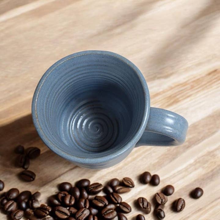 Blue ceramic mug on a wooden surface with coffee beans around it