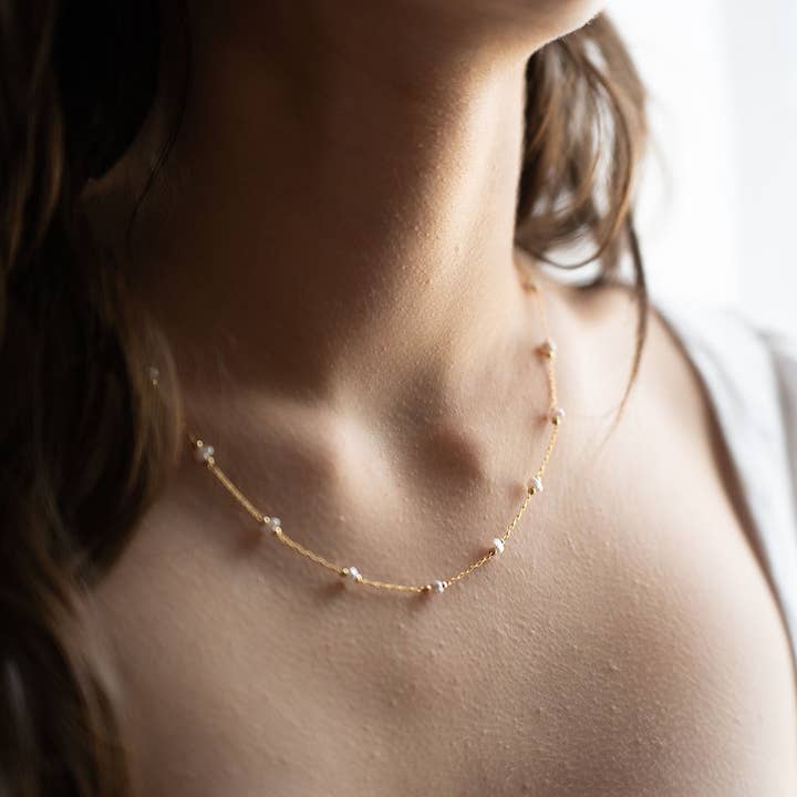 Close-up of a person wearing a delicate gold necklace with small pearls.