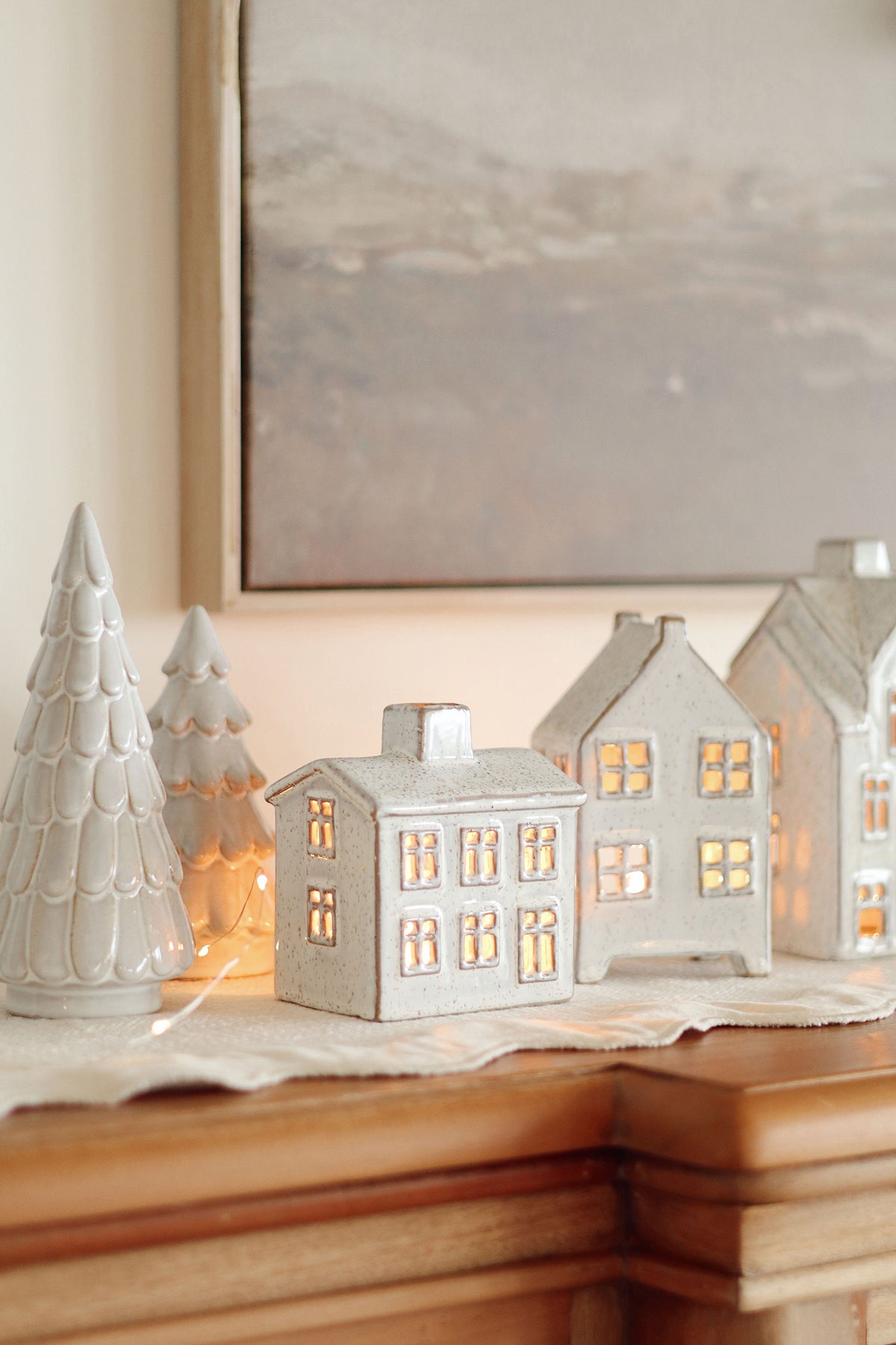 Set of ceramic house-shaped lanterns with glowing lights and ceramic trees on a surface.