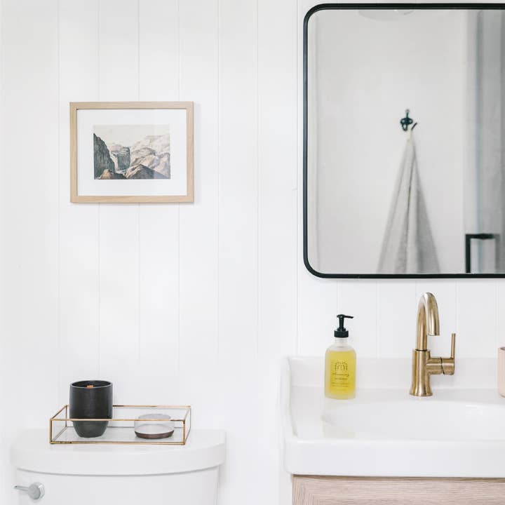 Bathroom with white vanity, gold faucet, and framed artwork on the wall.