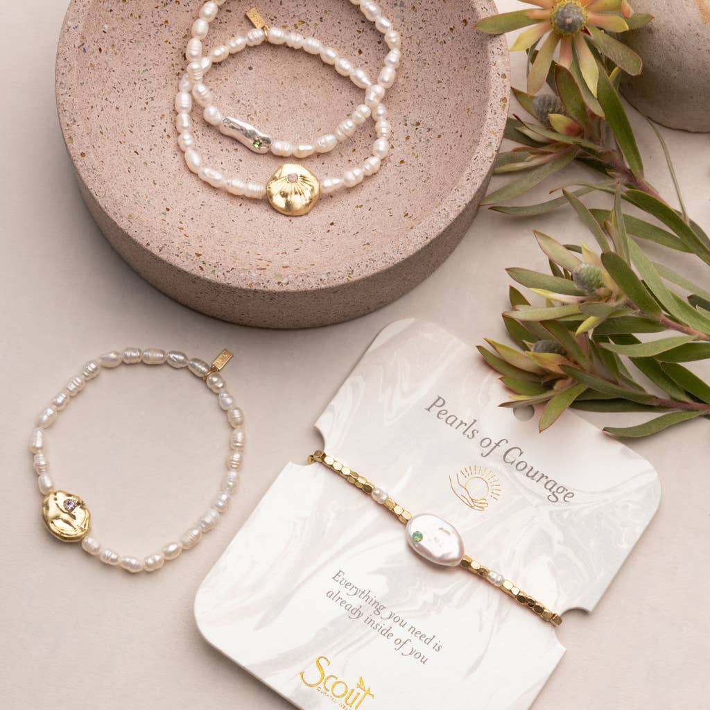 Pearl bracelets with gold accents on a beige surface with a 'Scout' branded card.