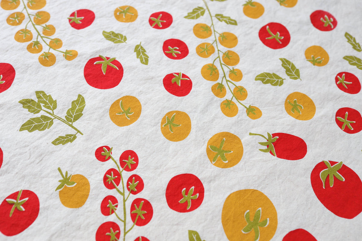 Close up of a white kitchen tea towel with a colorful print of red and yellow tomatoes and green leaves.