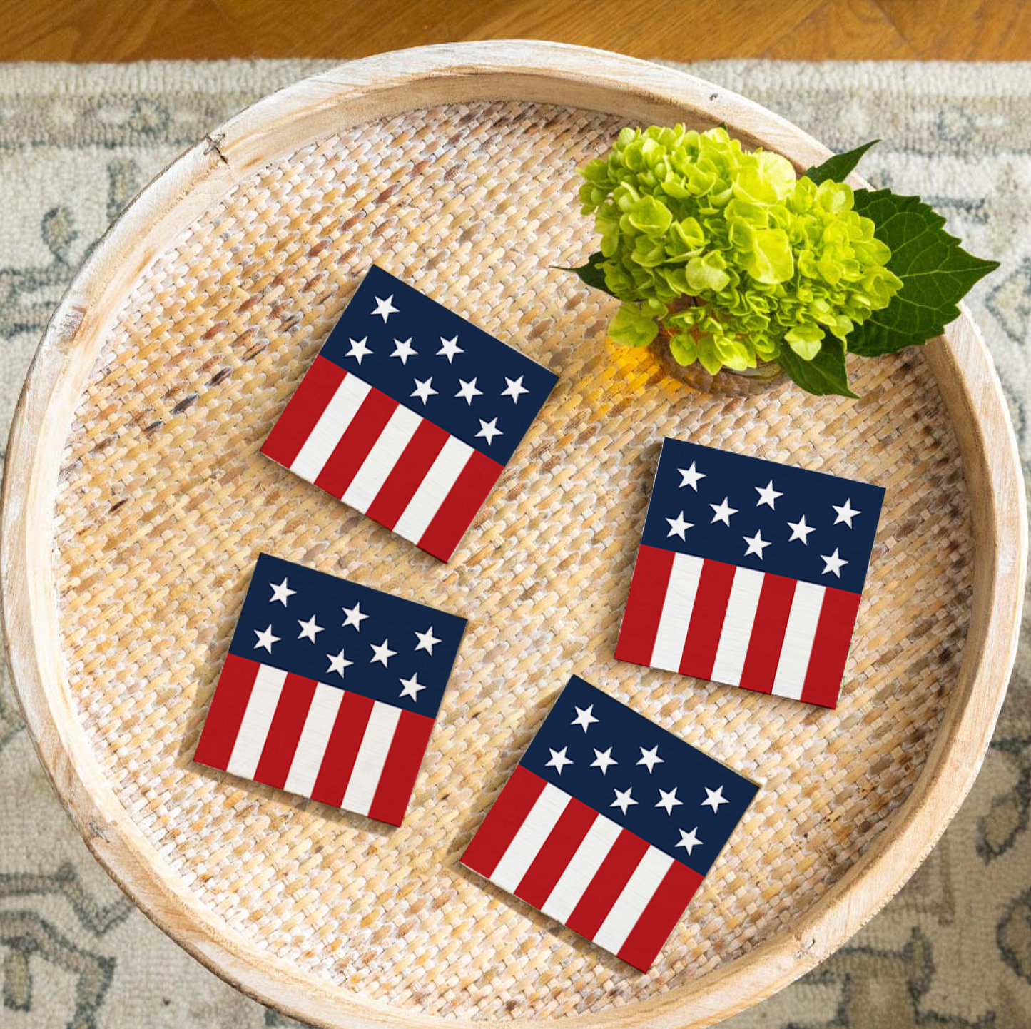 Four American flag coasters on a woven tray with green flowers.