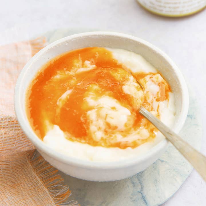 Bowl of yogurt and peach jam with a spoon on a light tabletop.