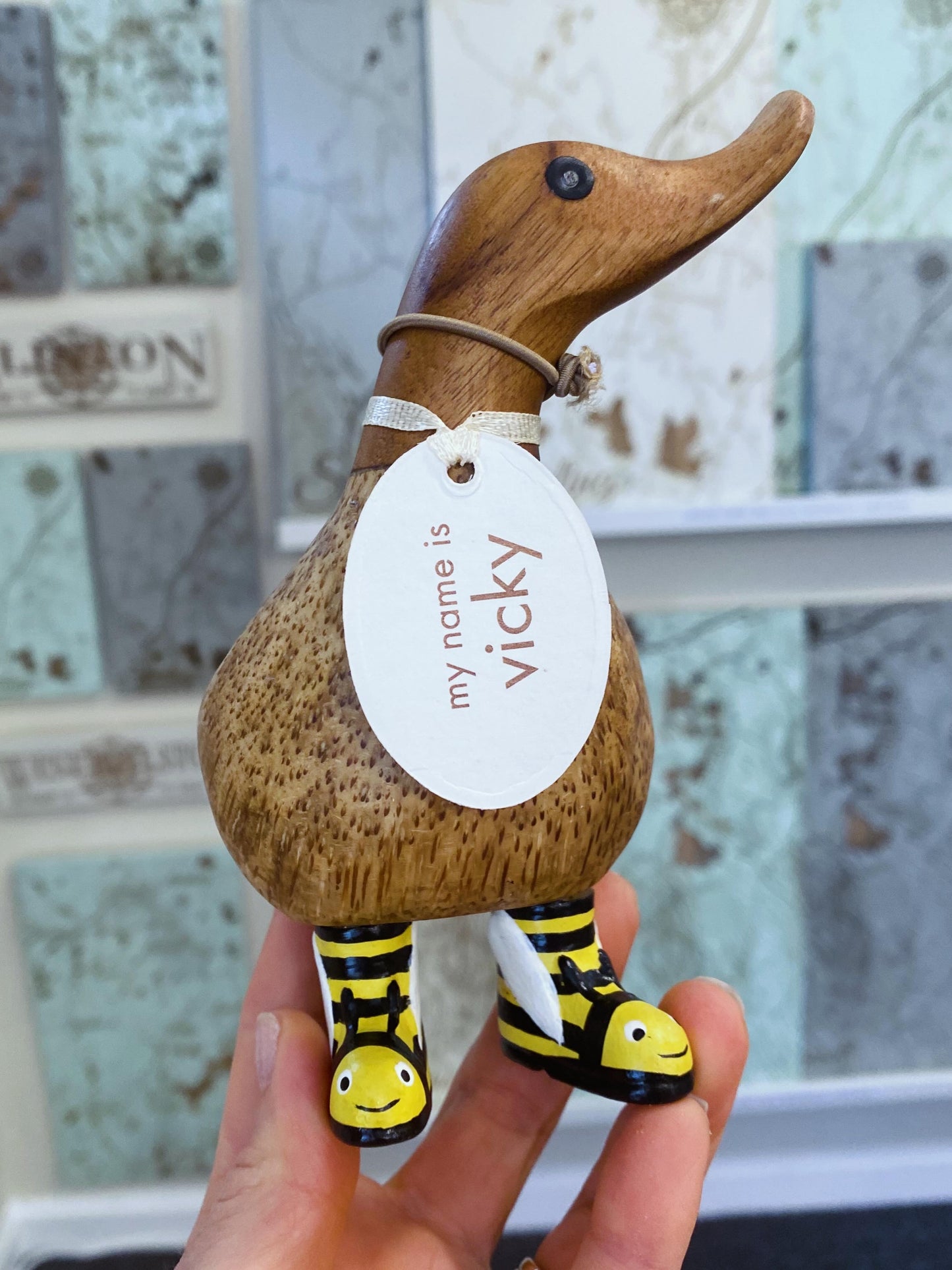 Wooden duck figurine with a 'my name is Vicky' tag held by a hand.