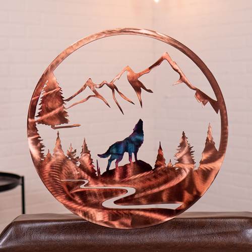 Decorative metal wall art with a wolf and mountain design on a wooden surface.