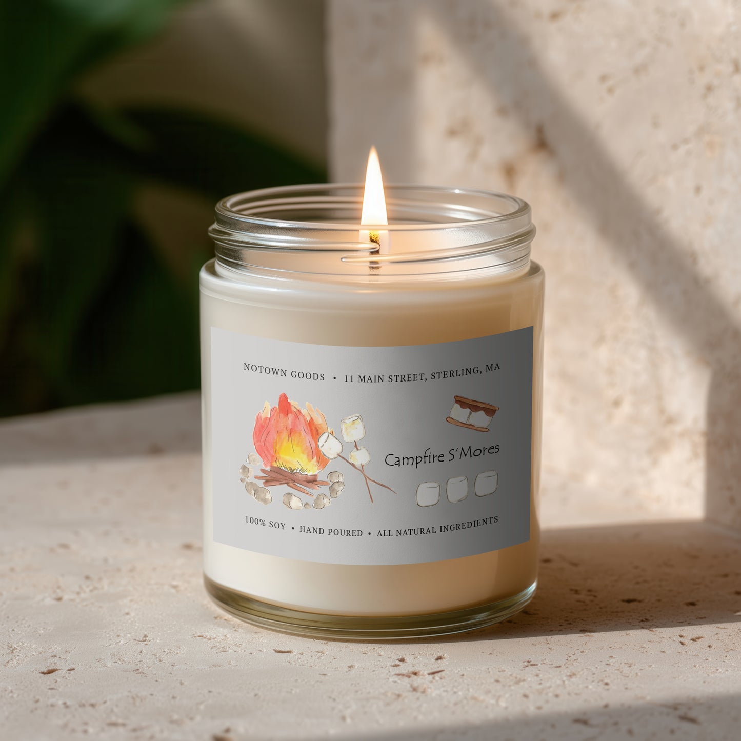 Clear jar candle with white wax and a decorative label on a blurred outdoor background.