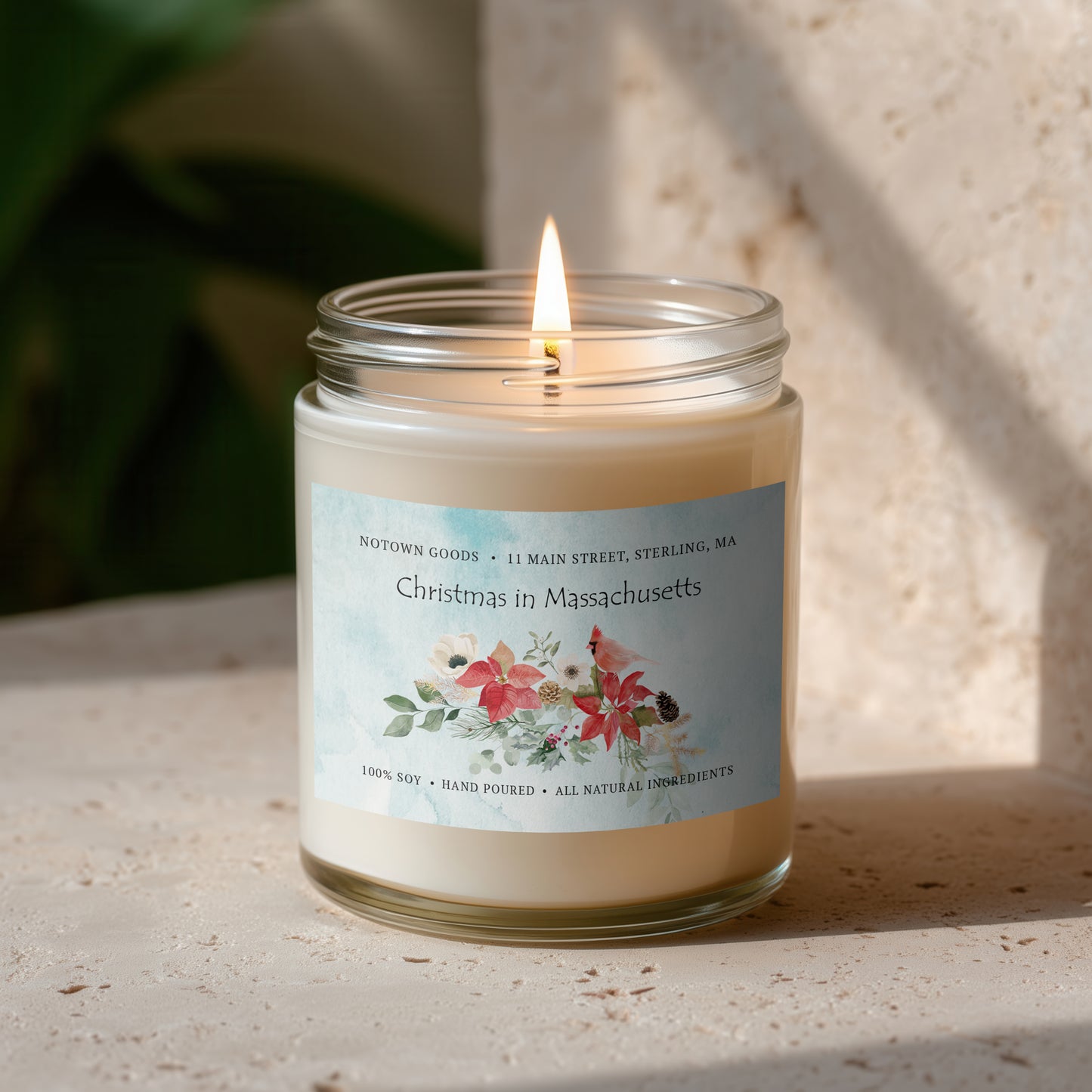 Clear jar candle with white wax and a decorative label on a blurred outdoor background.