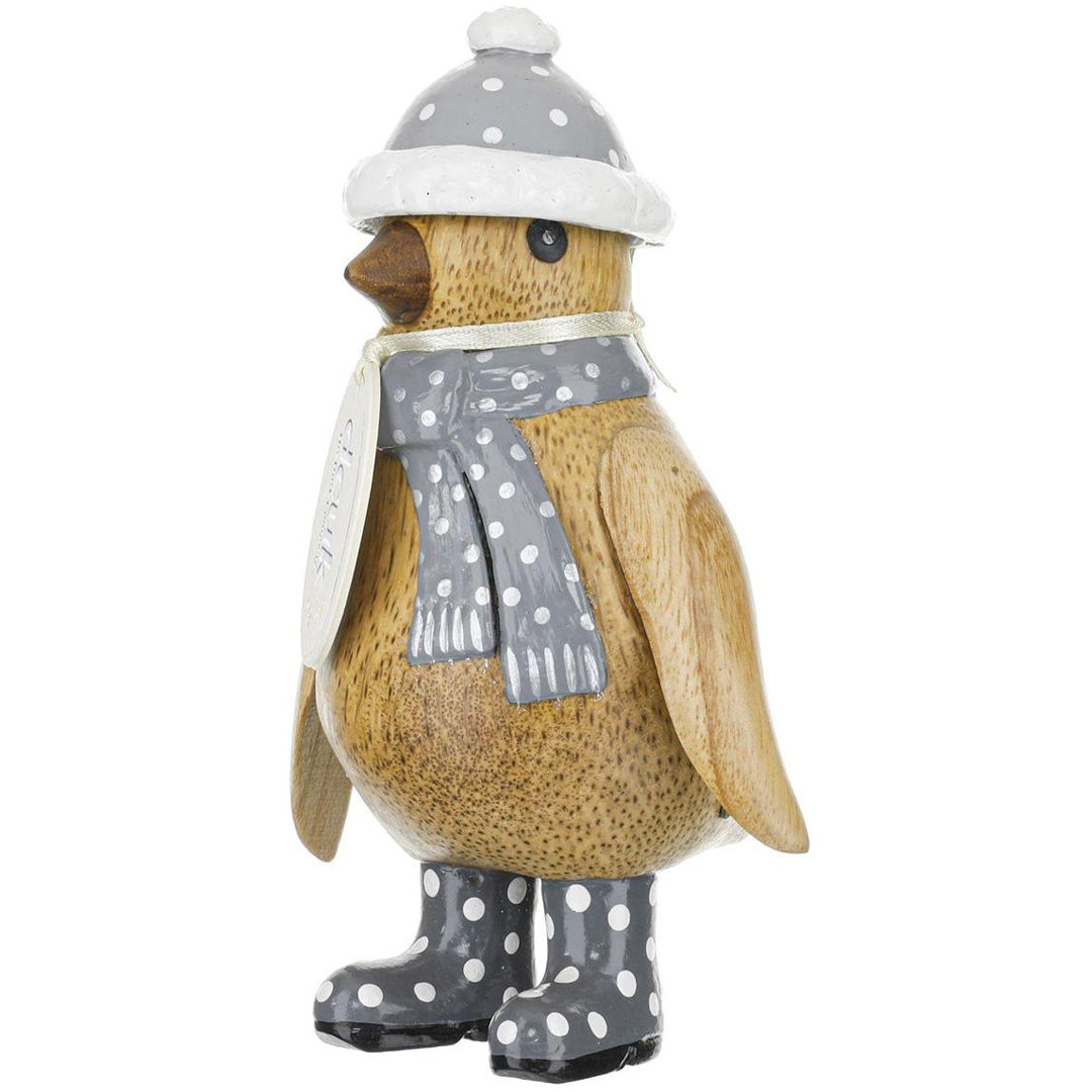 Wooden penguin figurine wearing a gray hat, scarf, and boots with white polka dots on a white background.