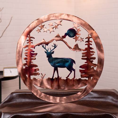 Decorative metal art piece with a deer, trees, and stars on a brown surface.