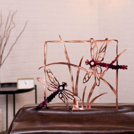 Decorative metal sculpture of dragonflies on a table with a neutral background