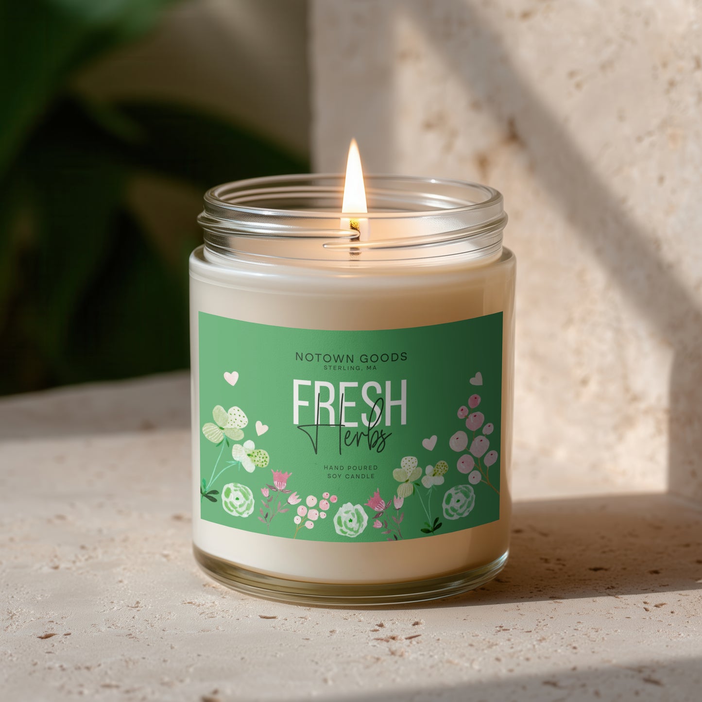 Clear jar candle with white wax and a decorative label on a blurred outdoor background.