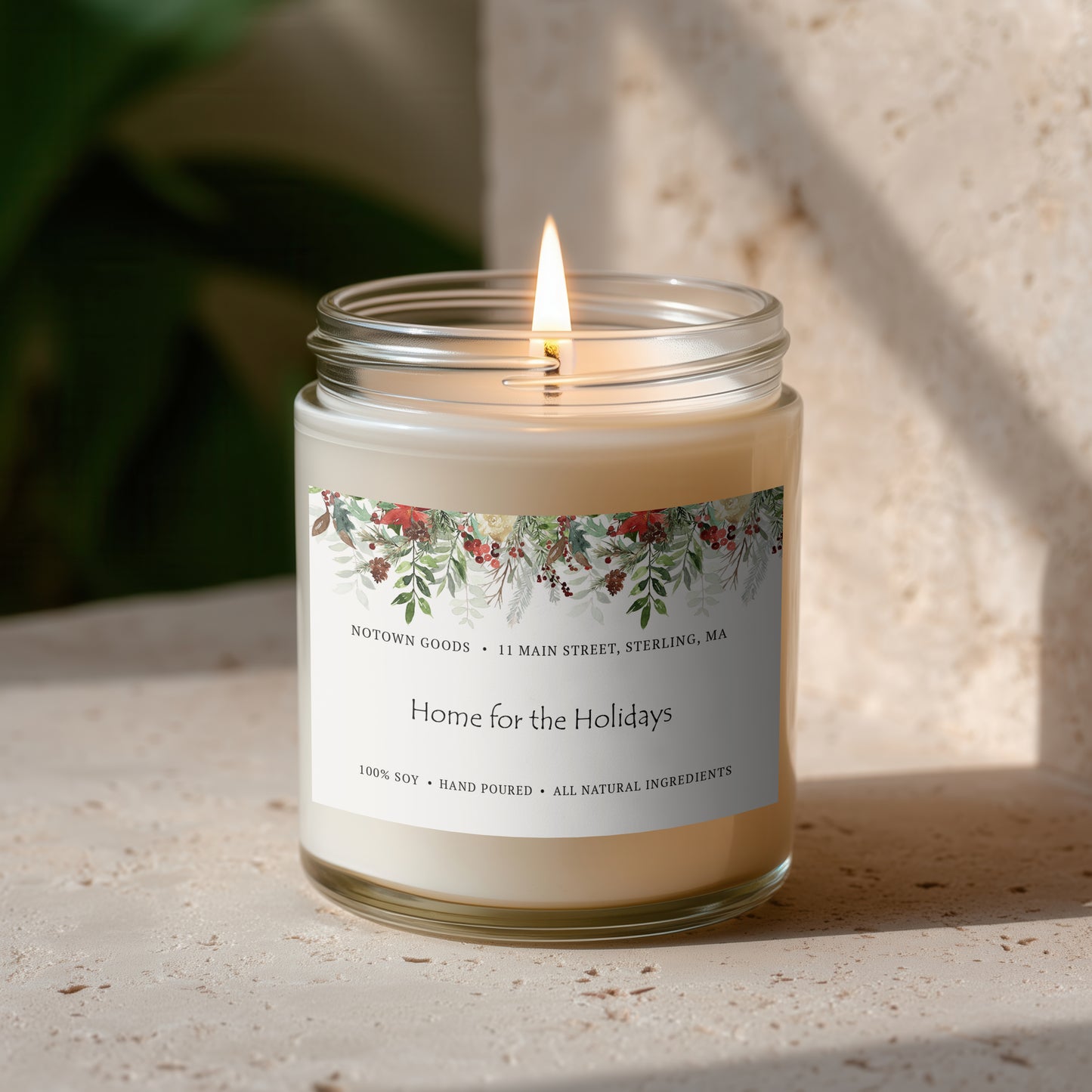 Clear jar candle with white wax and a decorative label on a blurred outdoor background.