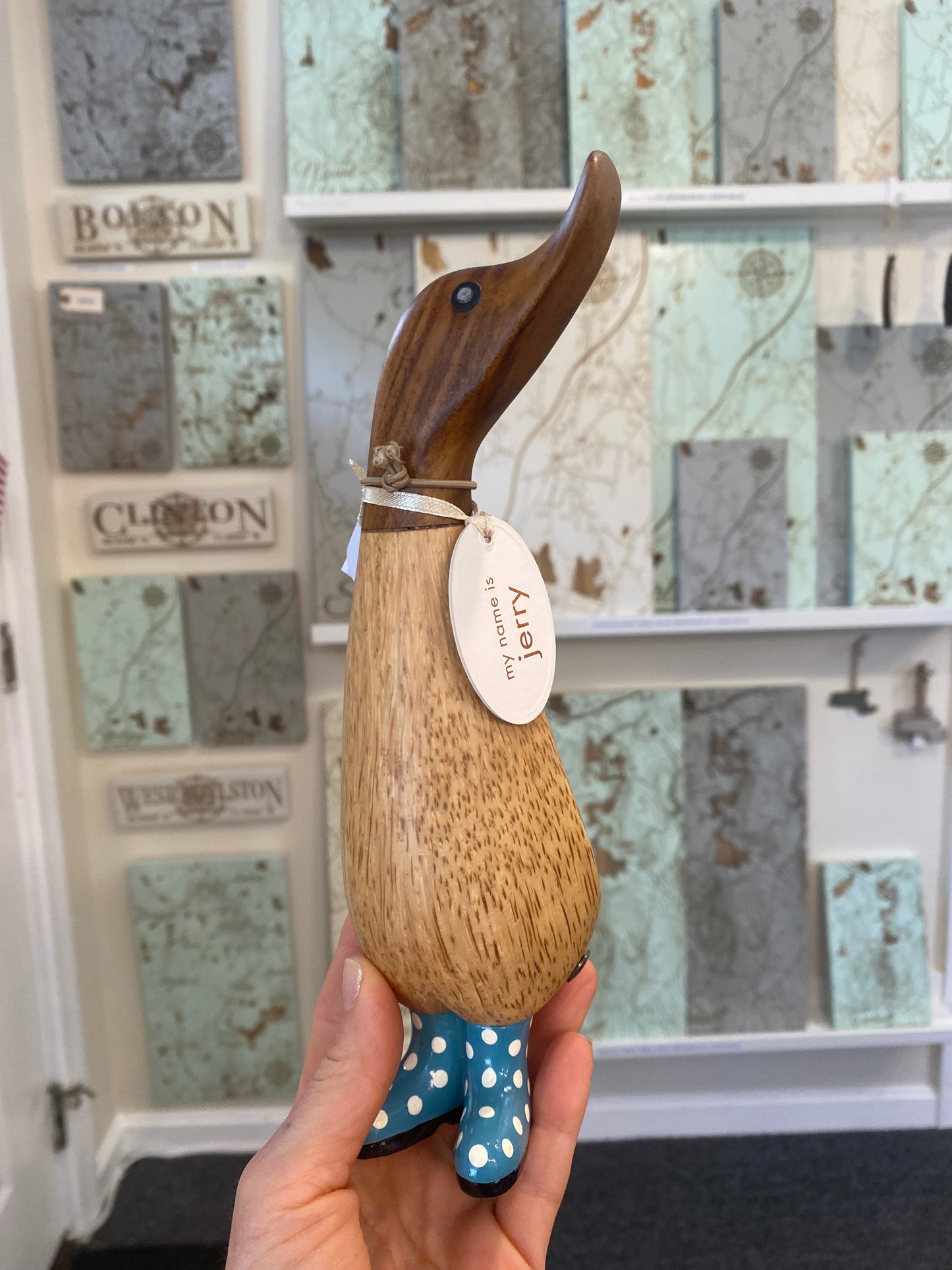Wooden duck held by a hand, against a decorative tile background.