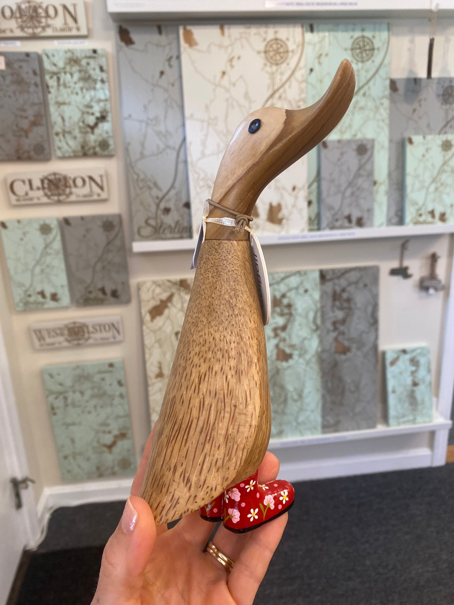 Hand holding a wooden duck with a decorative red boots against a map background