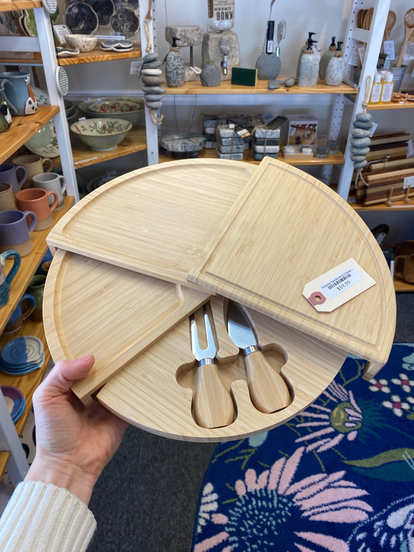 Wooden cheese board set with utensils held by a person in a store setting