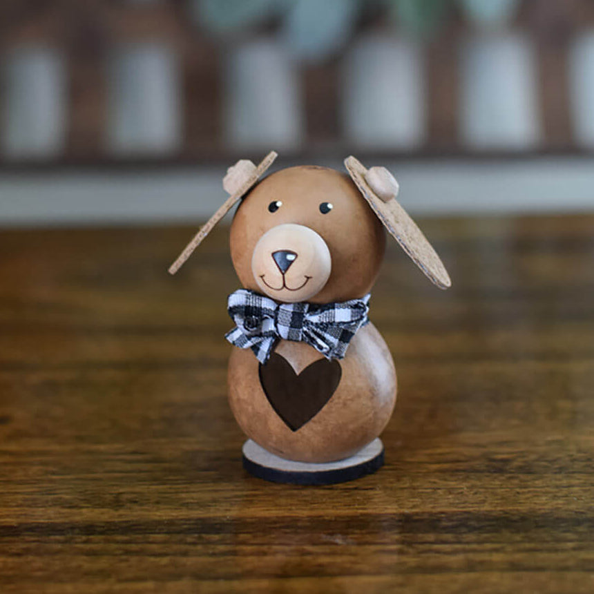 Dog shaped sculpture made from gourds with a black and white ribbon neck bow on a wooden surface.