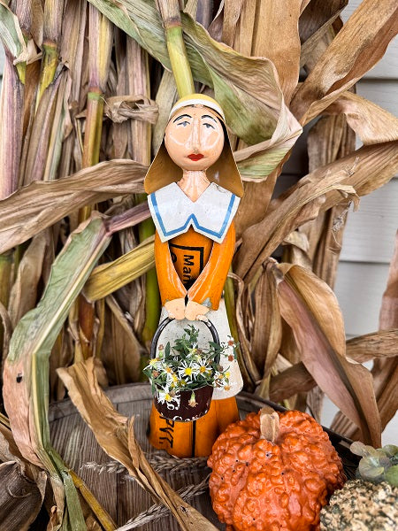 Decorative figurine of a woman holding flowers, surrounded by corn stalks and pumpkins.