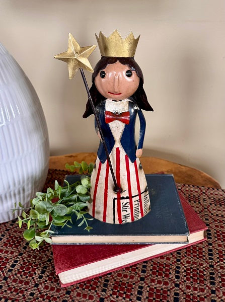 Decorative figurine of a woman with a crown and star, standing on books with a plant nearby.
