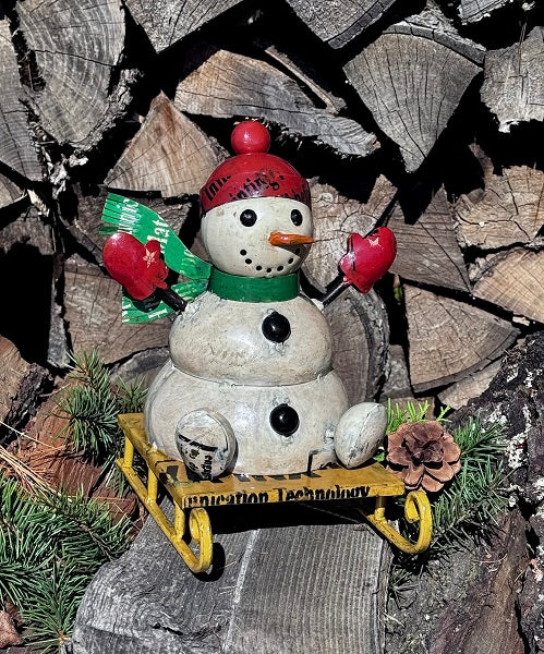 Decorative snowman figurine with a sled on a background of stacked logs.