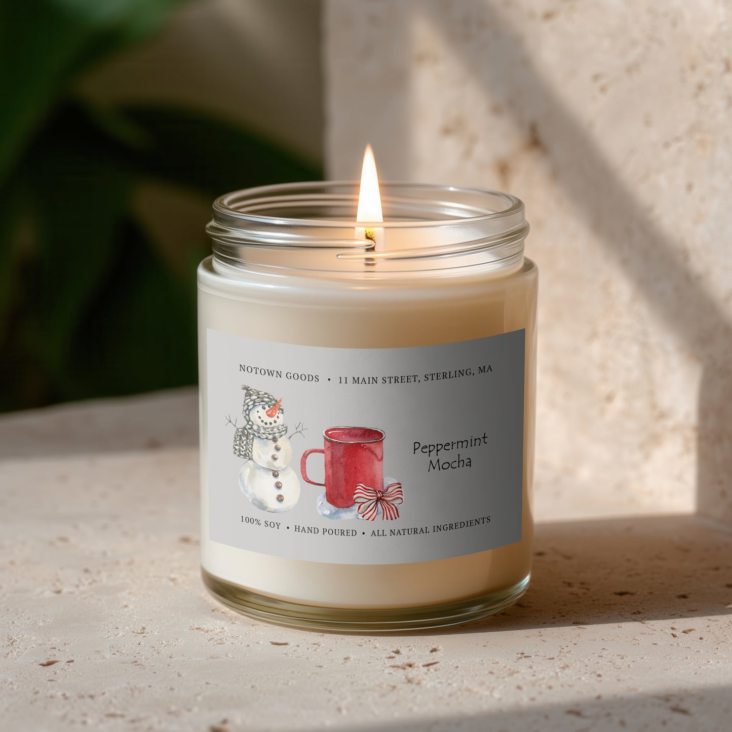 Clear jar candle with white wax and a decorative label on a blurred outdoor background.