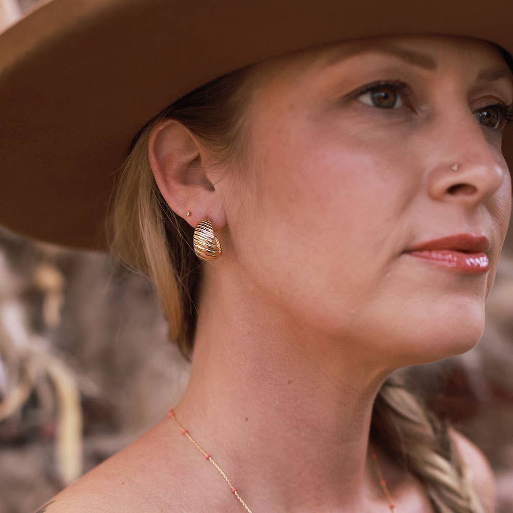 Woman wearing a wide-brimmed hat with gold earrings and a necklace.