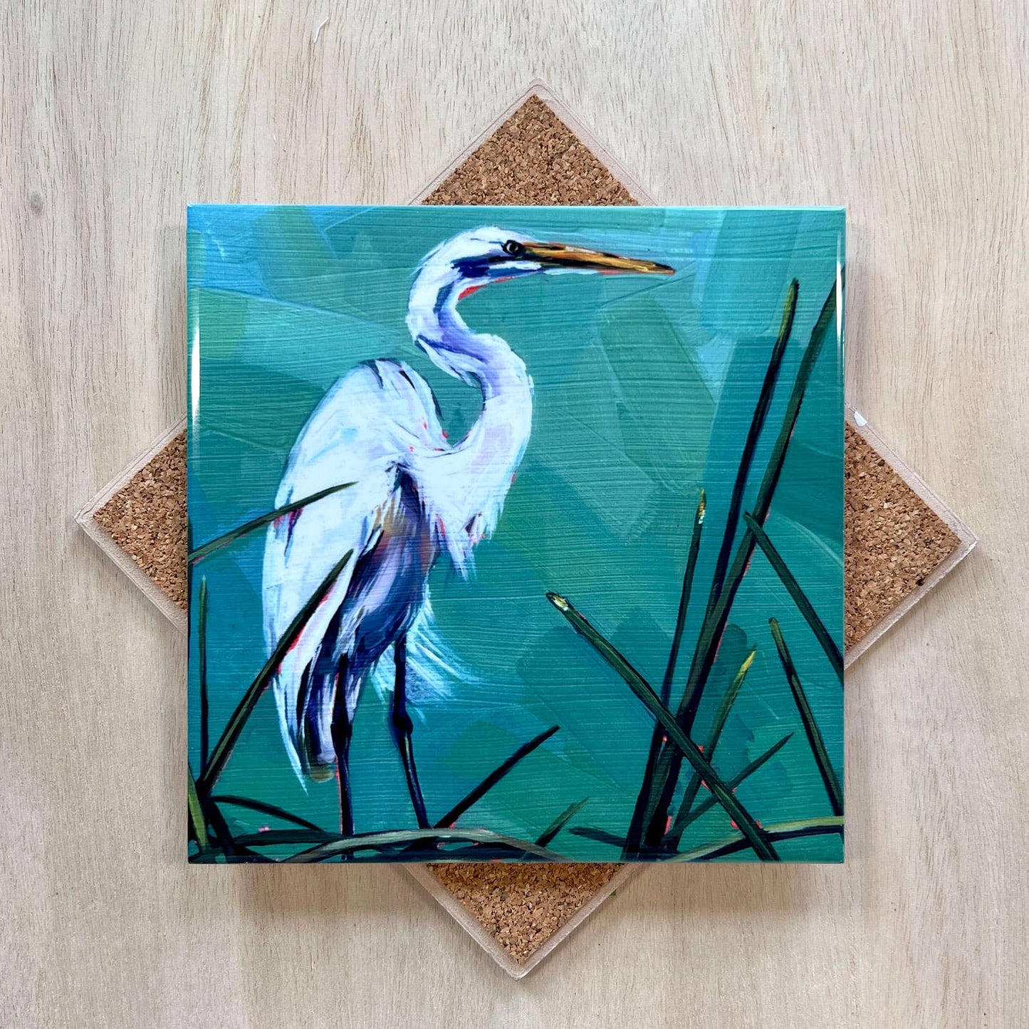 Coaster with a painting of a heron on a blue background, placed on a wooden surface.