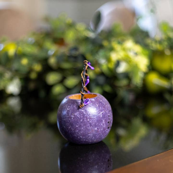 Purple decorative item on a reflective surface with blurred greenery in the background