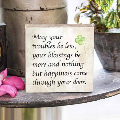 Decorative sign with inspirational quote and clover on a surface with flowers and plants in the background