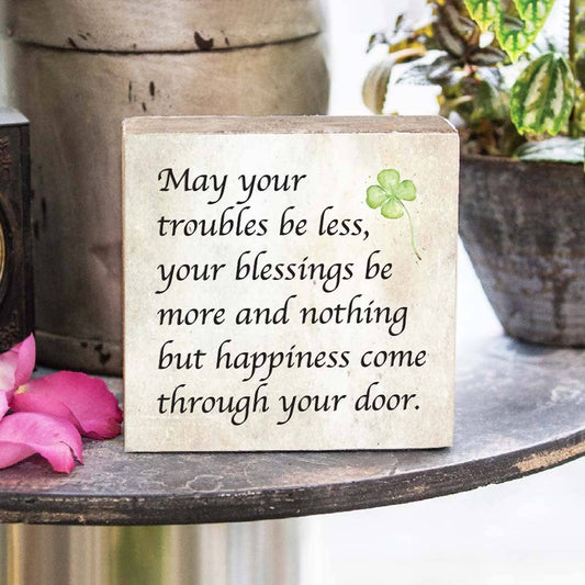 Decorative sign with inspirational quote and clover on a surface with flowers and plants in the background