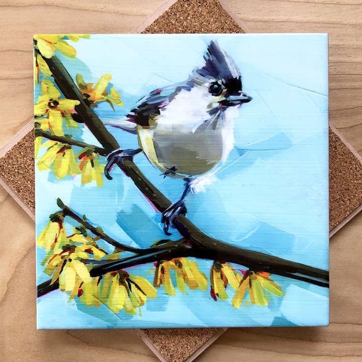 Trivet with a bird on a branch and yellow flowers against a blue sky.