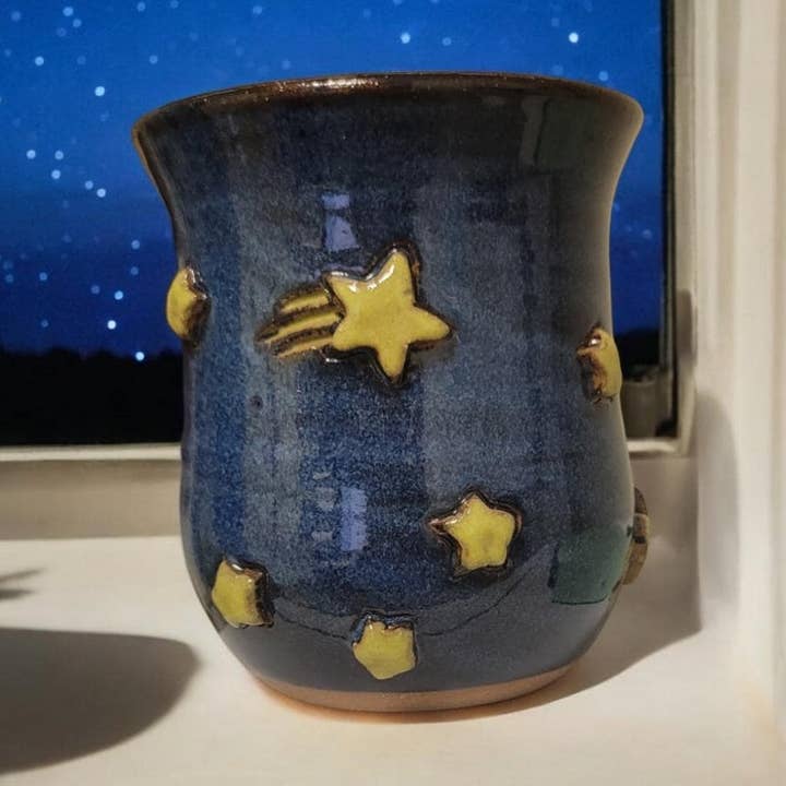 Blue ceramic mug with yellow star designs on a windowsill at night.