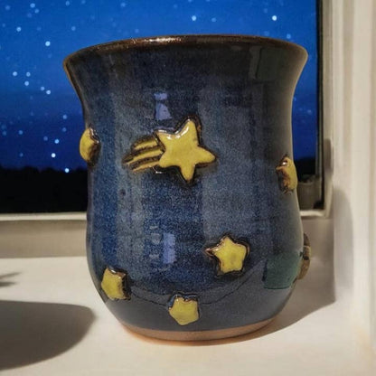 Blue ceramic mug with yellow star designs on a windowsill at night.