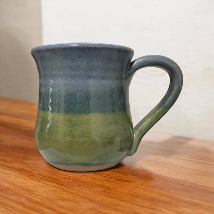 Green and blue ceramic mug on a wooden surface with a plain background