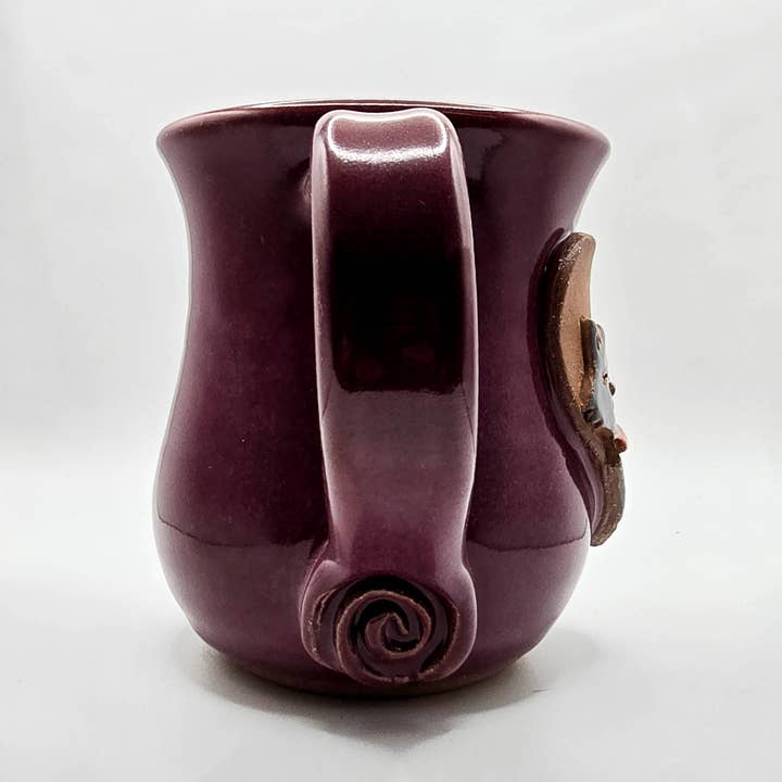 Purple ceramic mug with handle and decorative element on a white background