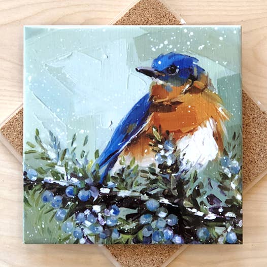 Trivet with a painting of a bluebird on a branch with berries on a wooden surface.
