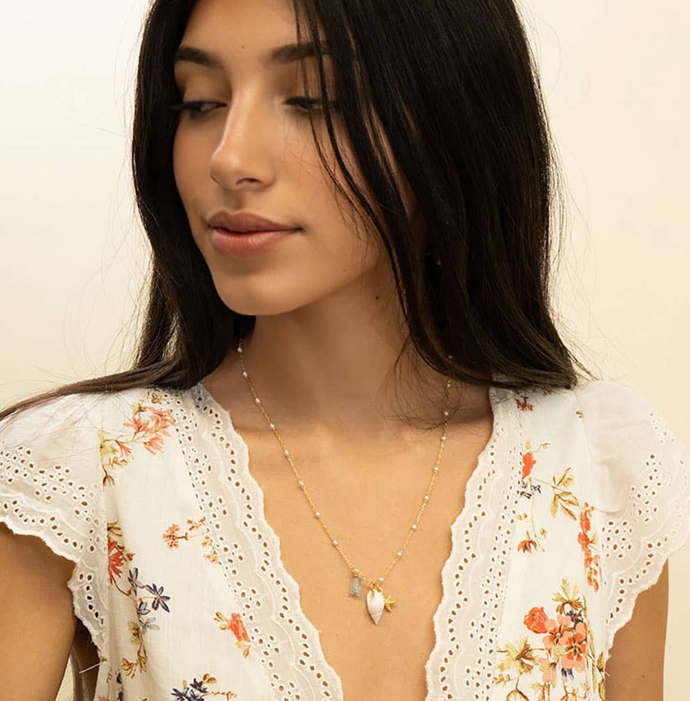 Woman wearing a floral blouse and necklace against a plain background