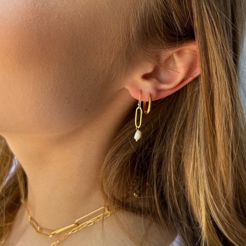Close-up of a person wearing gold hoop earrings with a pearl accent.
