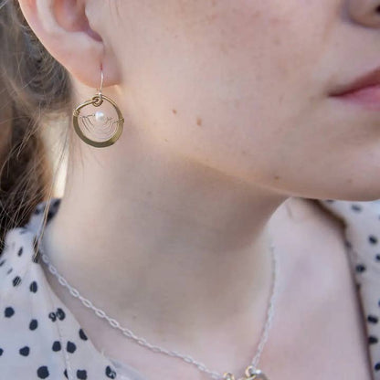 Close-up of a person wearing gold hoop earrings with a pearl accent.