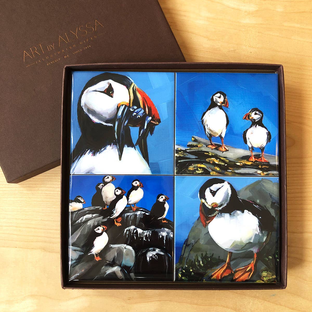 Box of ceramic coasters with puffin designs on a wooden surface