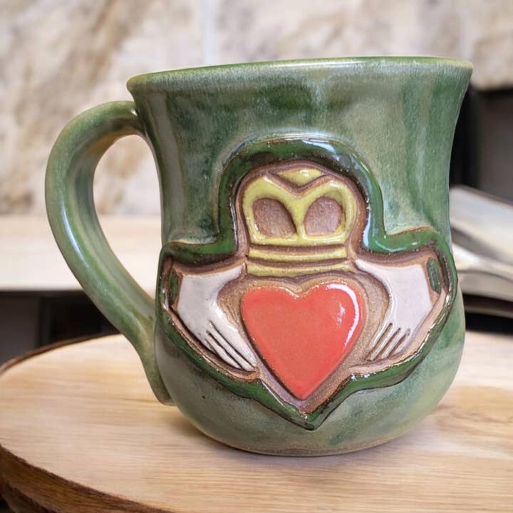 Green ceramic mug with a heart and crown design on a wooden surface