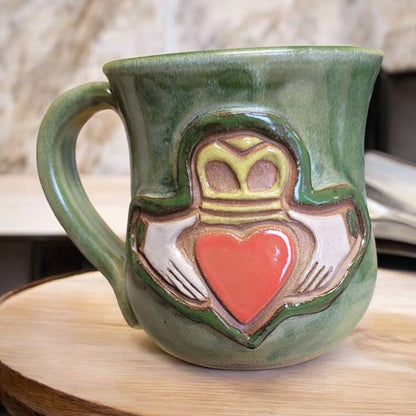 Green ceramic mug with a heart and crown design on a wooden surface
