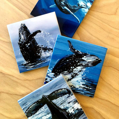 Four whale-themed coasters on a wooden surface
