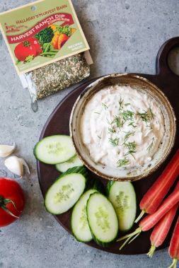 Dip in a bowl with vegetables on a plate, including cucumbers, carrots, and tomatoes, with a package of seasoning in the background.
