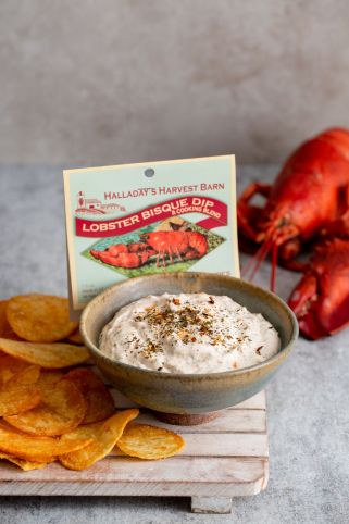Bowl of lobster bisque dip with chips and a lobster in the background, featuring Hallandale's Harvest Barn packaging.