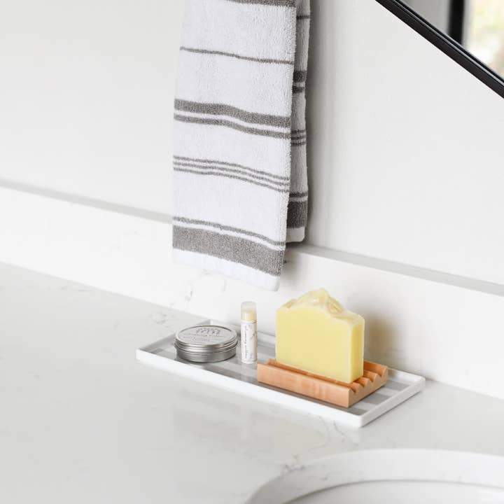 Bathroom setting with a soap dish holding a bar of soap, jar of salve, and a lip balm on a white surface.