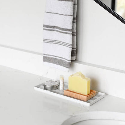 Bathroom setting with a soap dish holding a bar of soap, jar of salve, and a lip balm on a white surface.