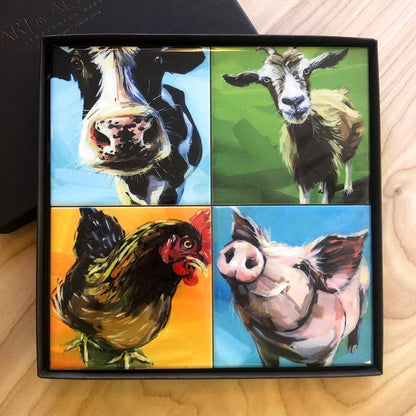 Four coasters with animal paintings (cow, goat, rooster, pig) in a gift box on a wooden surface.