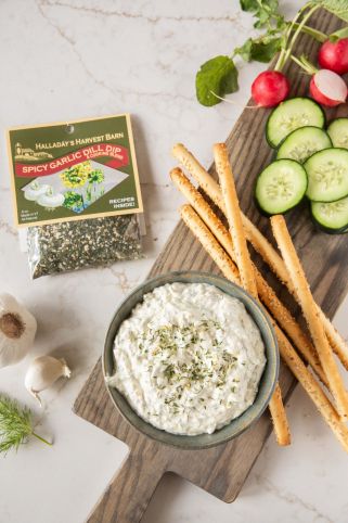 Dip with crackers and vegetables on a wooden board with a package of herbs in the background.