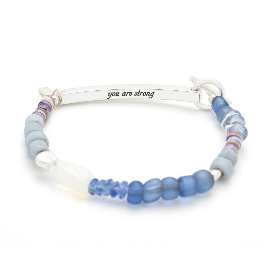 Bracelet with blue and purple beads and a silver bar with 'you are strong' engraving on a white background